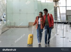 medcare vacances - stock photo romantic trip happy african couple hug walk with baggage in empty airport terminal safe flight 1960952029